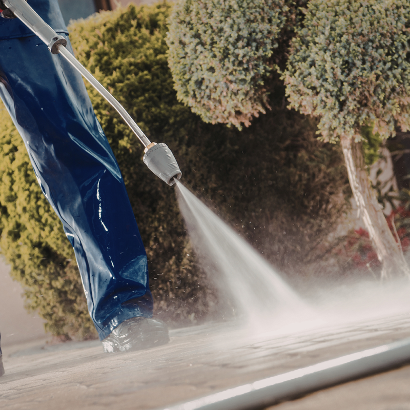 Homeowner pressure washing a residential driveway and home exterior in spring — Ontario exterior cleaning guide